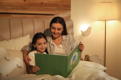 Photo of Little girl with mother reading book in bedroom lit by night lamp