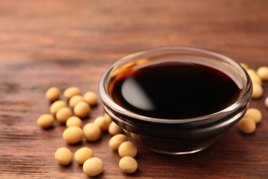 Photo of Soy sauce in bowl and soybeans on wooden table, closeup