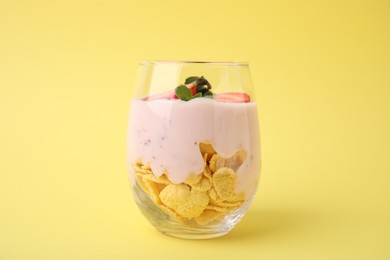 Photo of Glass with yogurt, strawberries and corn flakes on yellow background