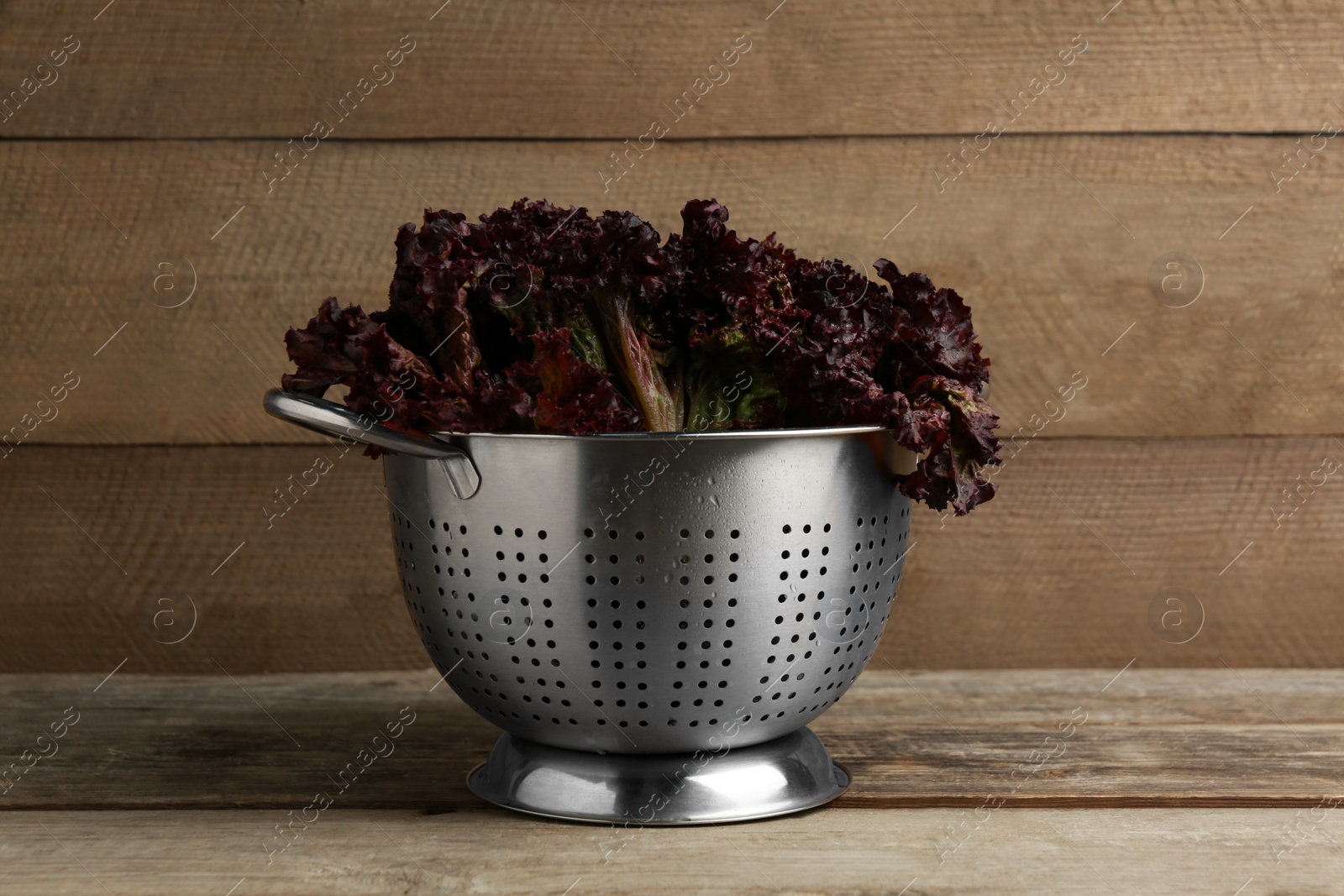 Photo of Colander with red coral lettuce on wooden table