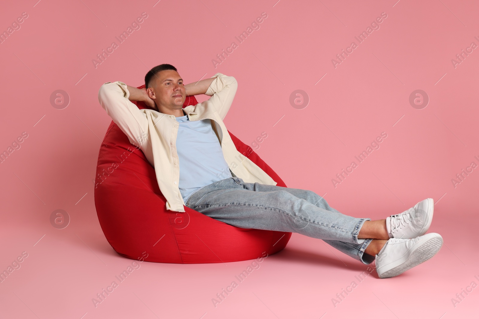 Photo of Handsome man on red bean bag chair against pink background