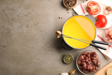 Photo of Flat lay composition with oil pot, meat fondue ingredients and space for text on grey background