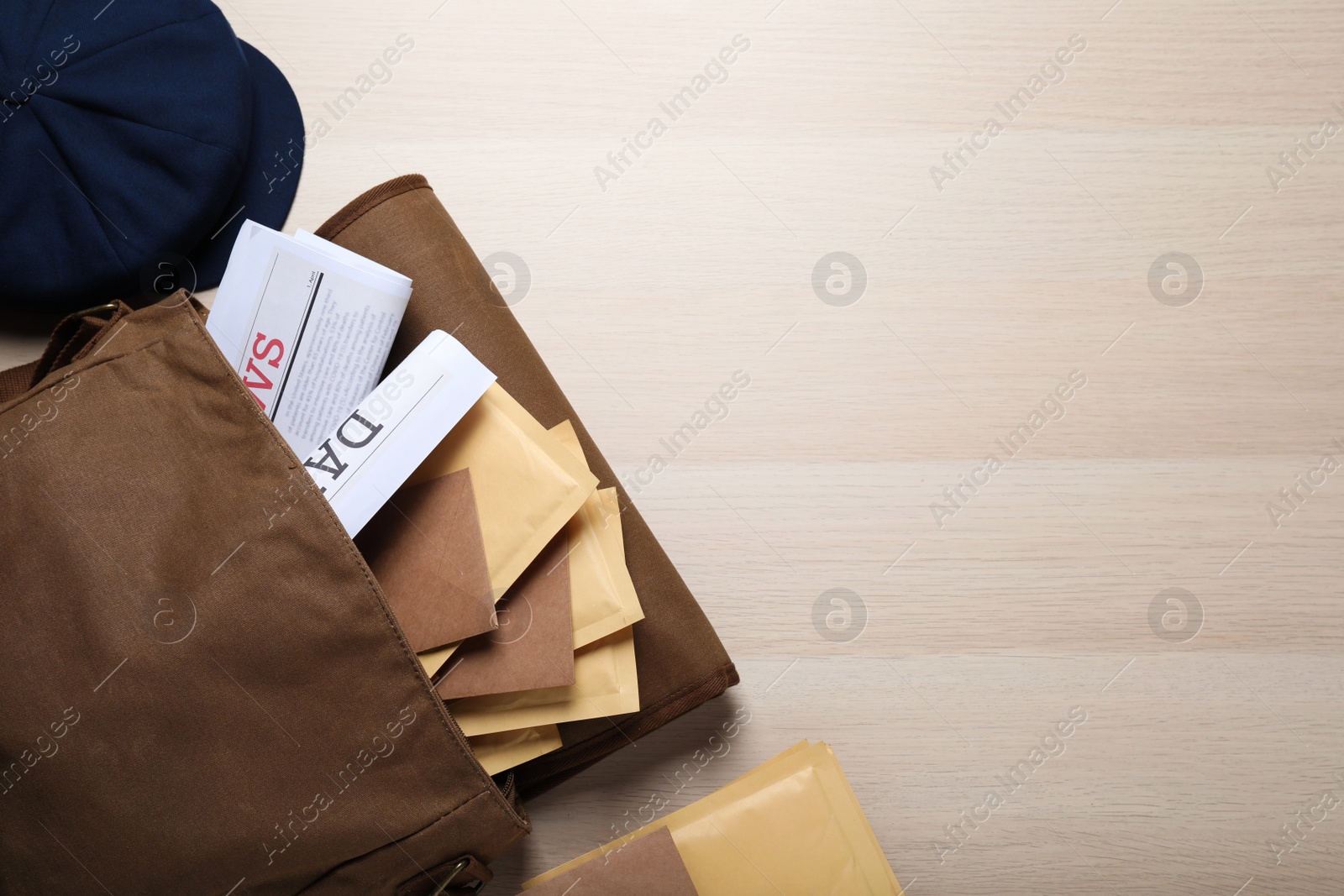 Photo of Brown postman's bag with envelopes, newspapers and hat on wooden table, flat lay. Space for text