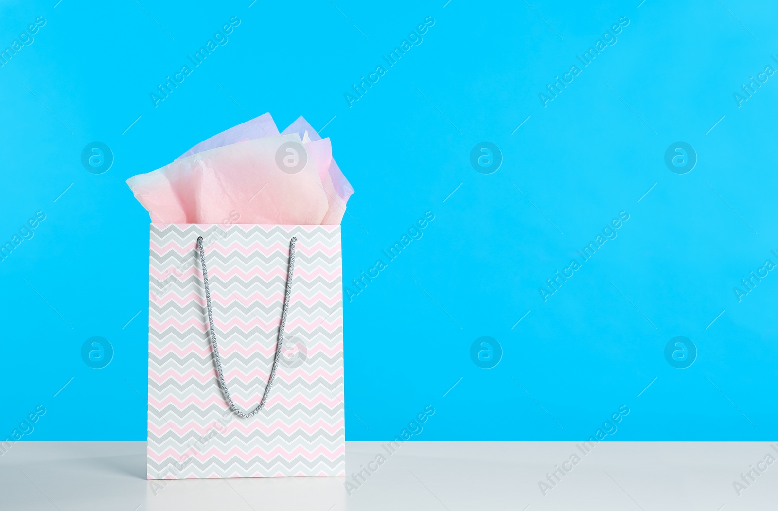 Photo of Gift bag with paper on white table against light blue background. Space for text