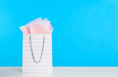 Photo of Gift bag with paper on white table against light blue background. Space for text