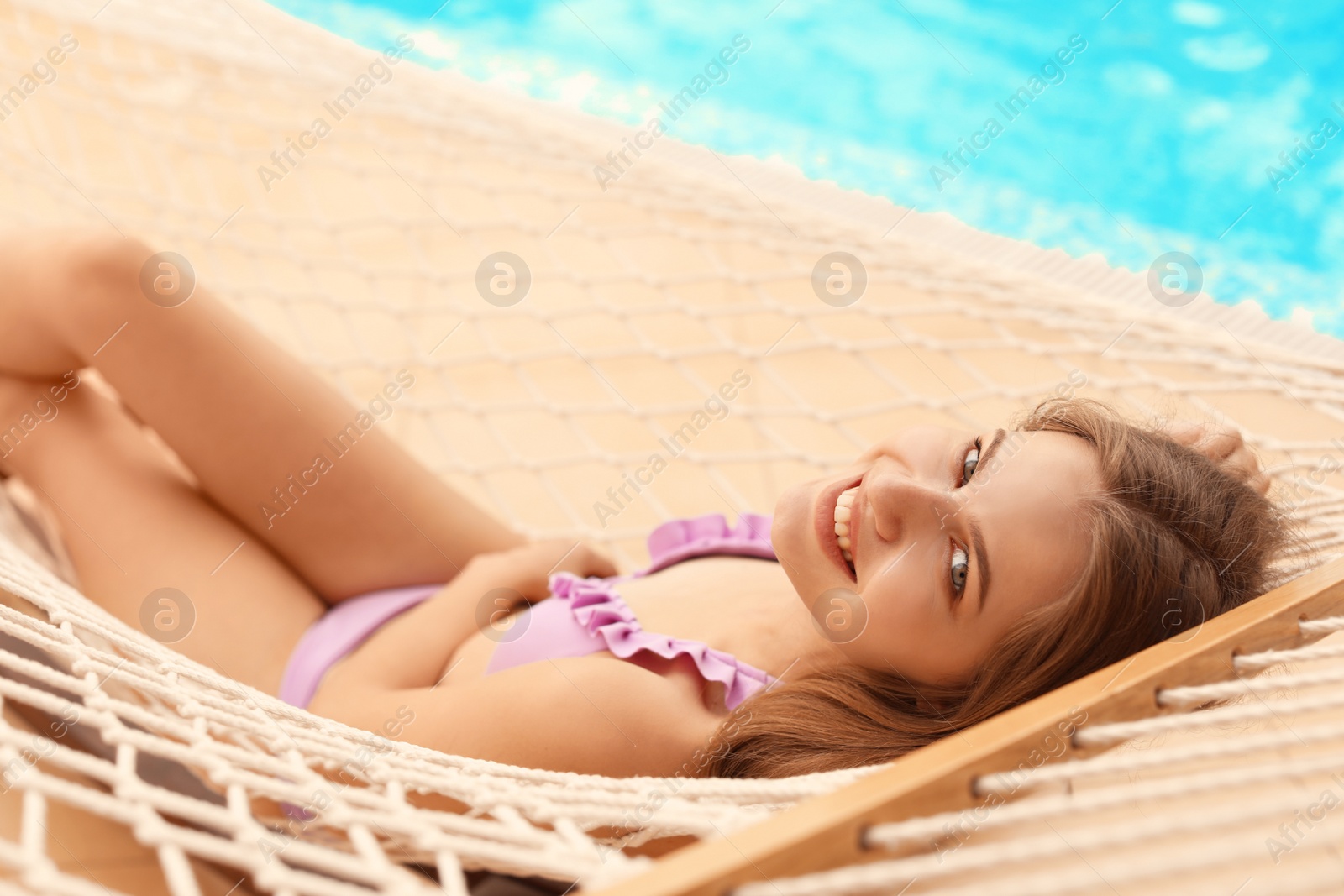 Photo of Young woman resting in hammock near pool