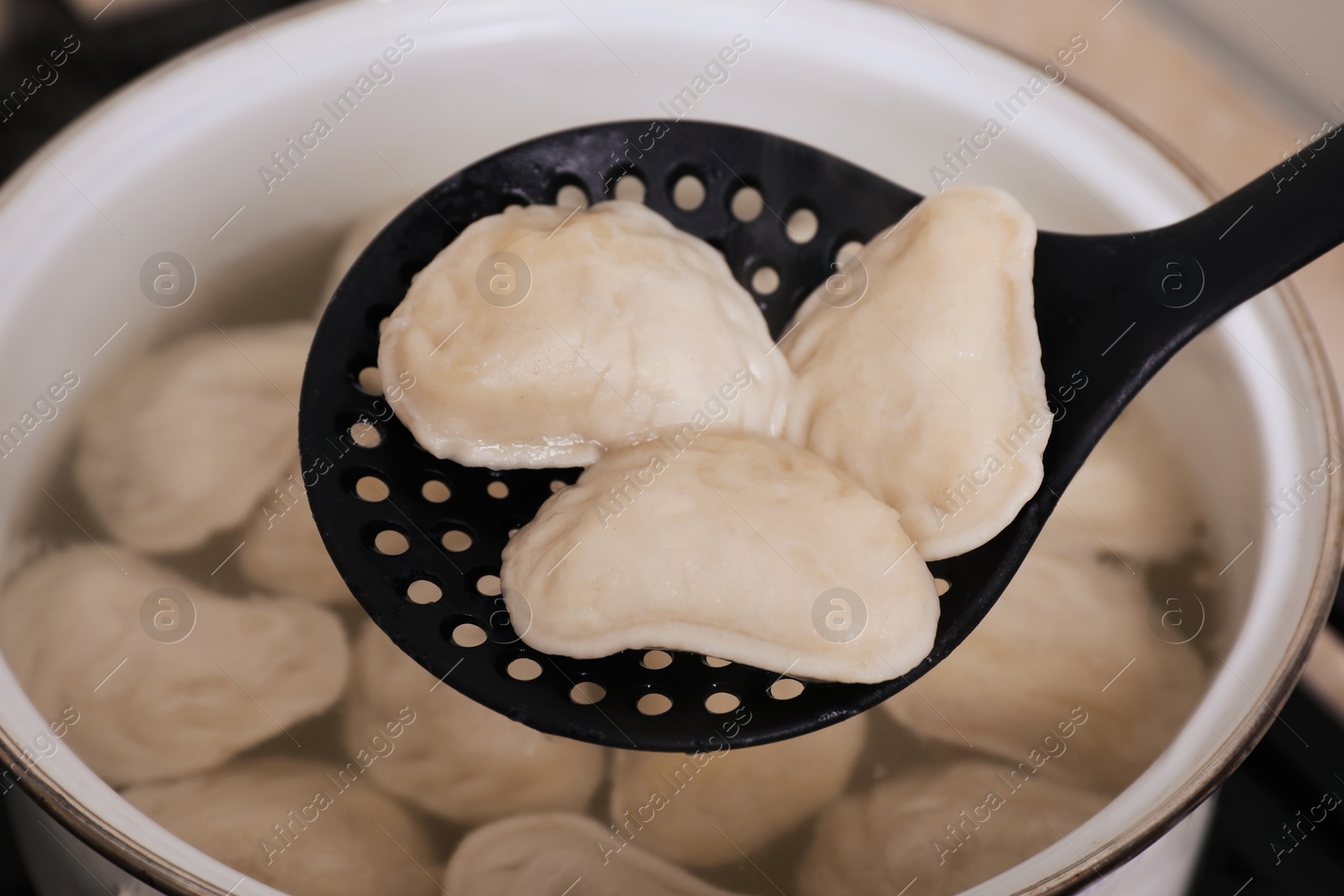 Photo of Dumplings (varenyky) with tasty filling on skimmer over pot, closeup