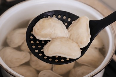 Dumplings (varenyky) with tasty filling on skimmer over pot, closeup