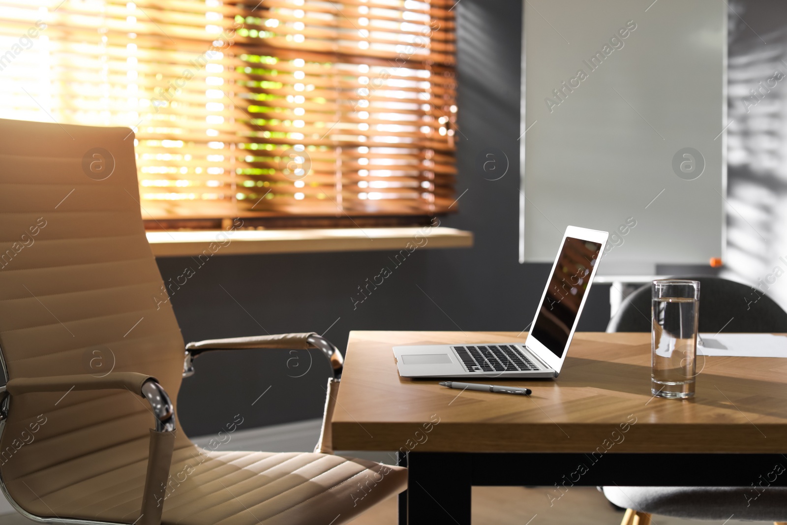 Photo of Laptop and glass of water on wooden table in modern office