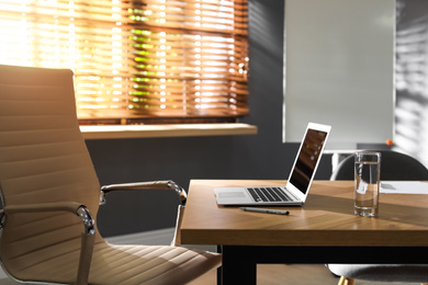 Laptop and glass of water on wooden table in modern office