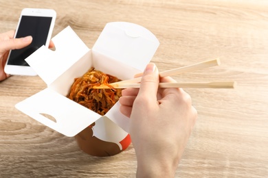 Photo of Woman eating Chinese noodles at wooden table, closeup. Food delivery