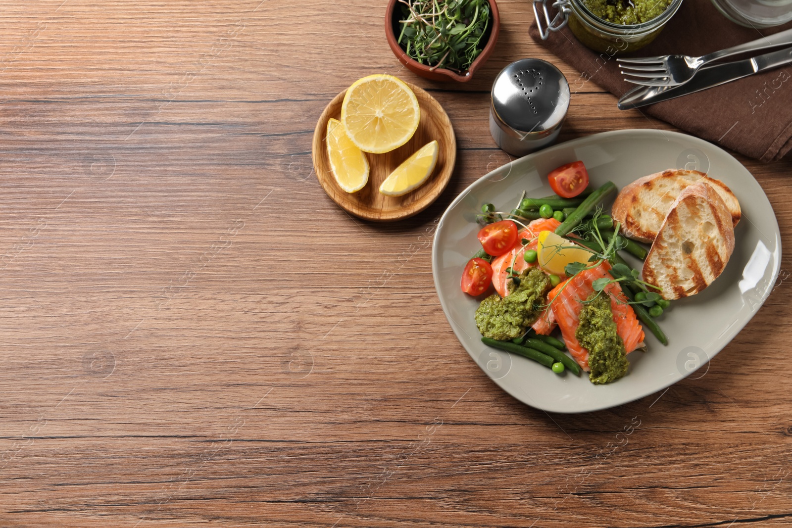 Photo of Tasty cooked salmon with pesto sauce served on wooden table, flat lay. Space for text