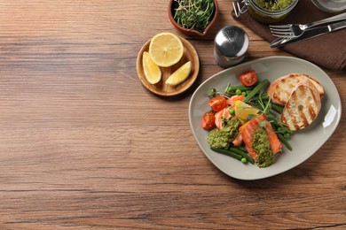 Photo of Tasty cooked salmon with pesto sauce served on wooden table, flat lay. Space for text