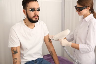 Photo of Young man undergoing laser tattoo removal procedure in salon