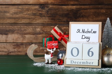 Saint Nicholas Day. Block calendar with date December 06, card and festive decor on green wooden table, space for text