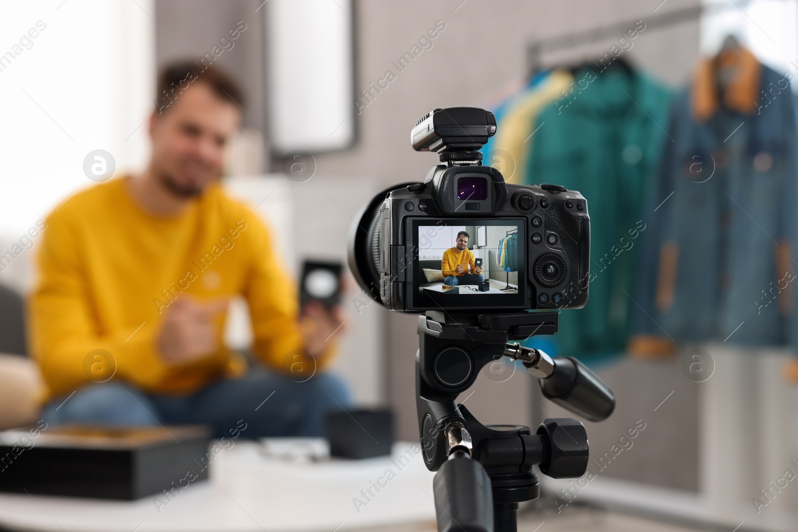 Photo of Fashion blogger showing wristwatch while recording video at home, focus on camera