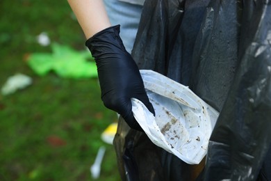 Photo of Woman with plastic bag collecting garbage on green grass, closeup
