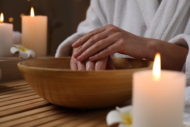 Photo of Woman soaking her hands in bowl of water at wooden table, closeup. Spa treatment