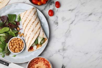 Photo of Plate with hummus wrap and vegetables on white marble table, flat lay. Space for text