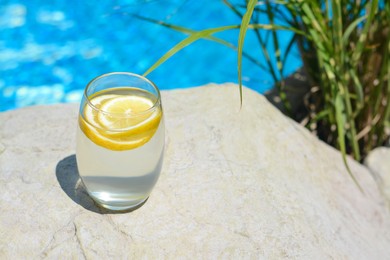 Photo of Refreshing water with lemon on rock outdoors, space for text