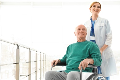 Photo of Nurse assisting elderly man in wheelchair indoors. Space for text
