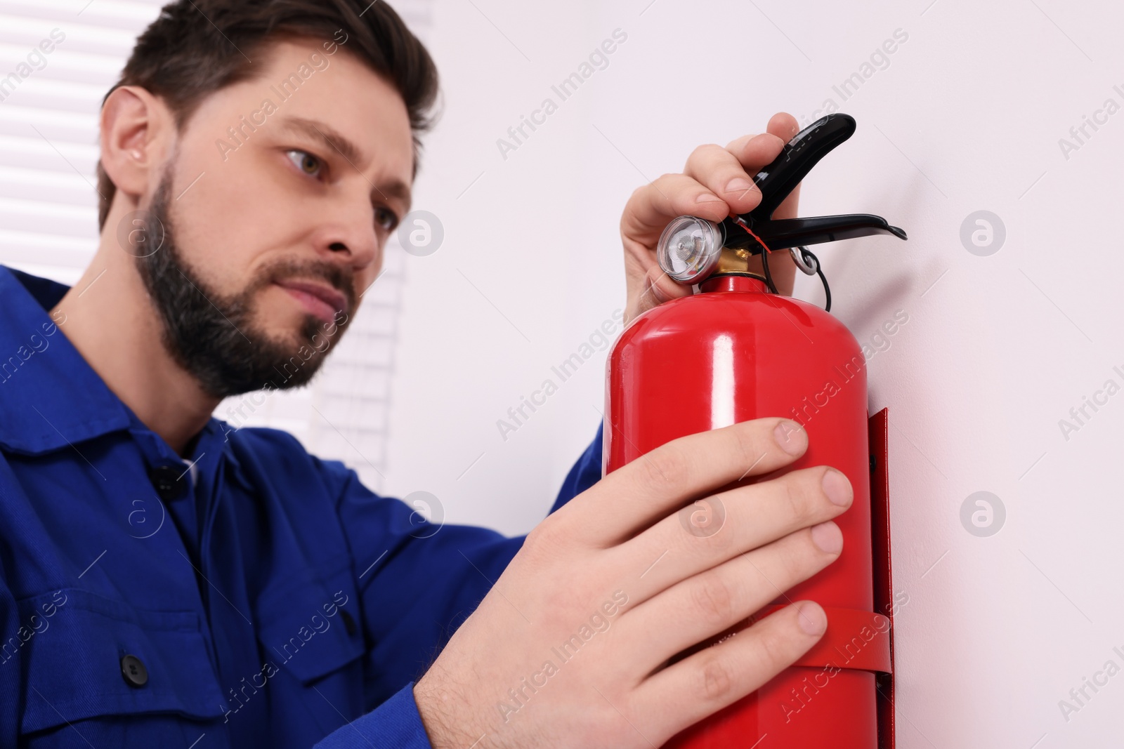 Photo of Man checking fire extinguisher indoors, selective focus