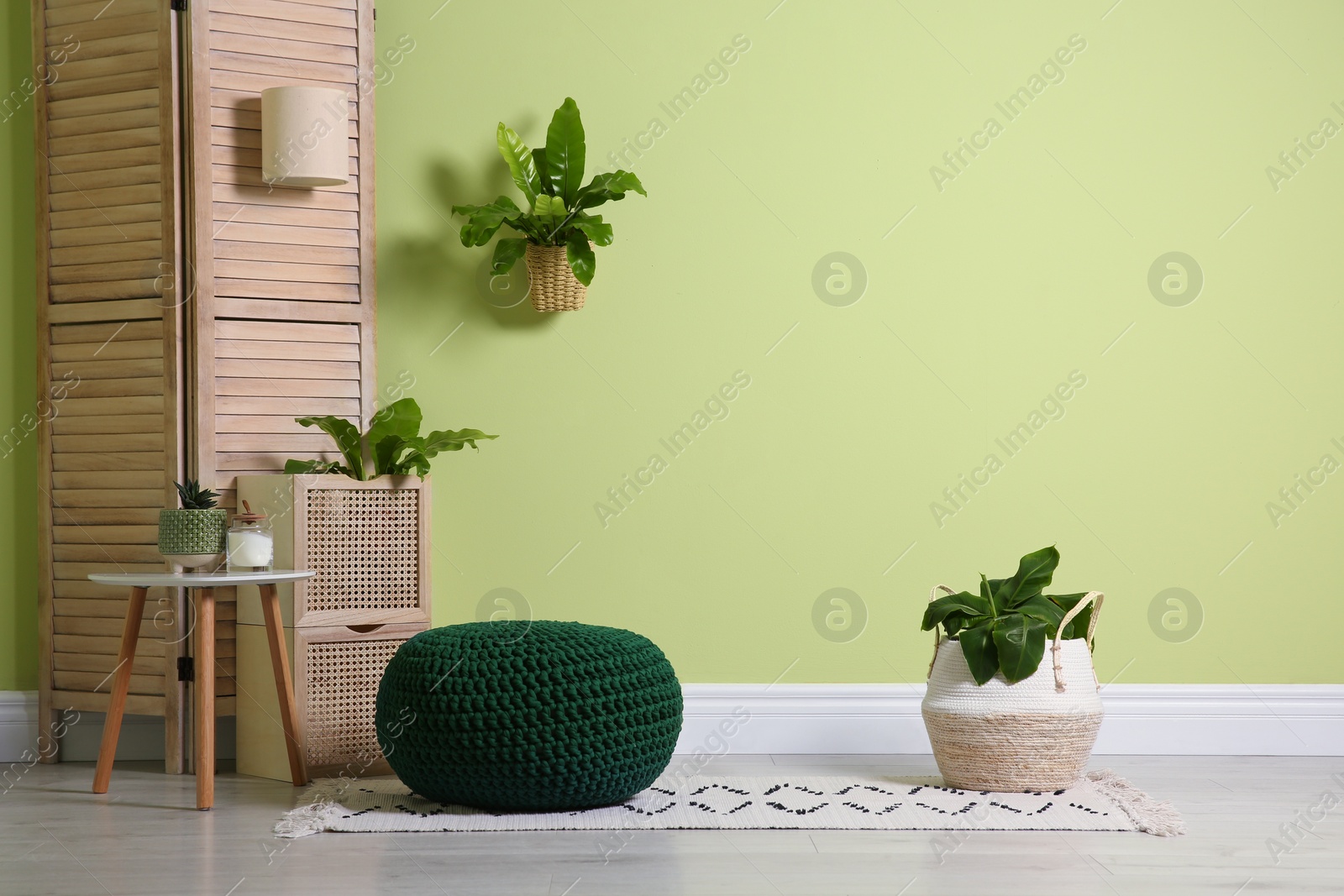 Photo of Stylish room interior with comfortable knitted pouf and plants near light green wall