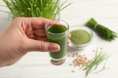 Woman holding glass of wheat grass drink at white table, closeup