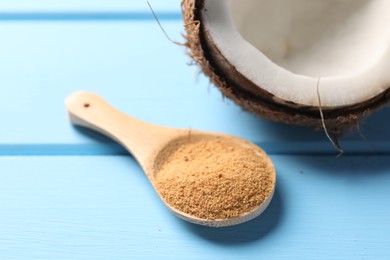 Photo of Spoon with coconut sugar and half of fruit on light blue wooden table, closeup