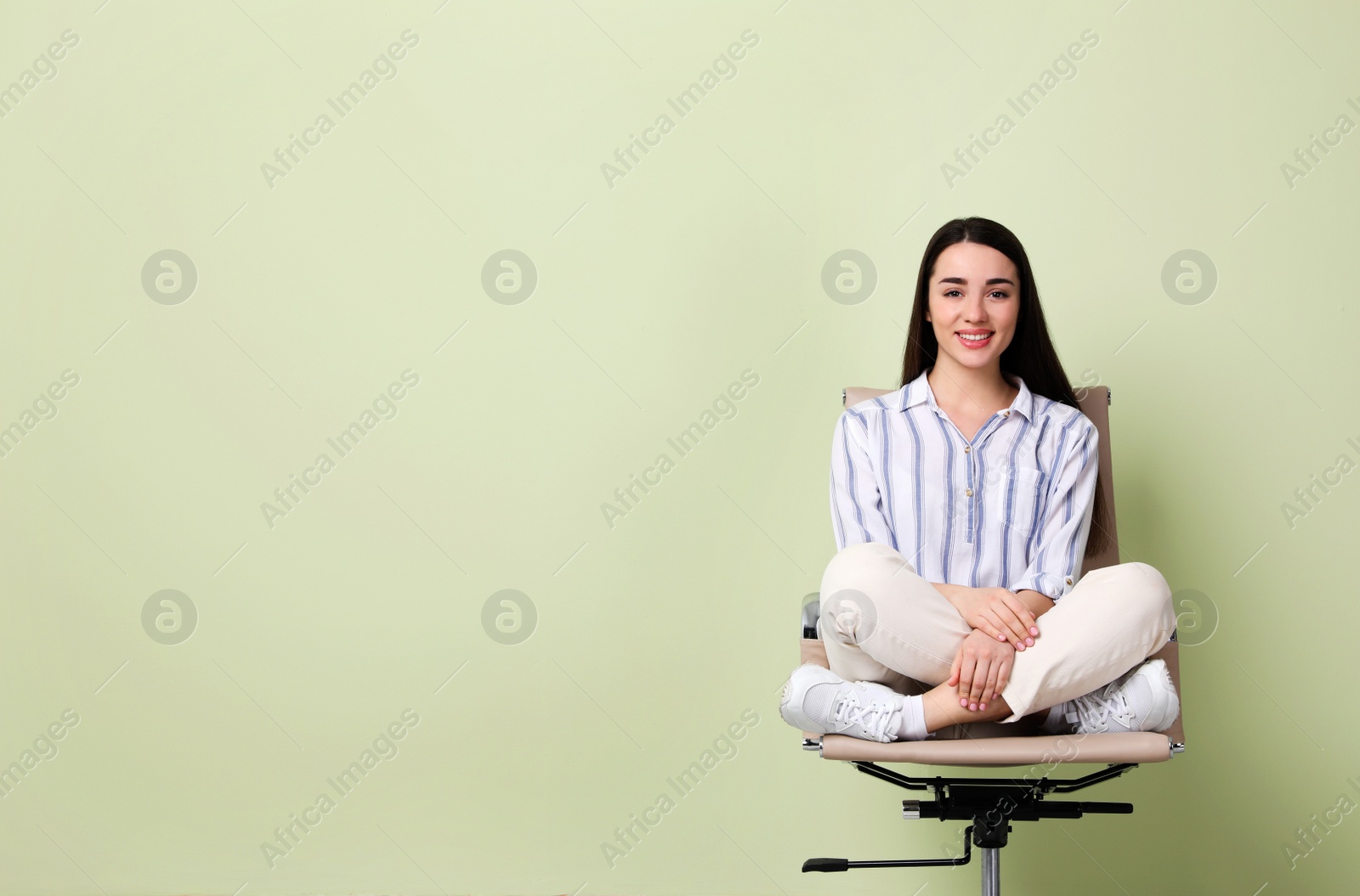 Photo of Young woman sitting in office chair on green background, space for text