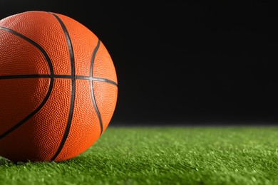 Photo of Basketball ball on green grass against black background, closeup. Space for text