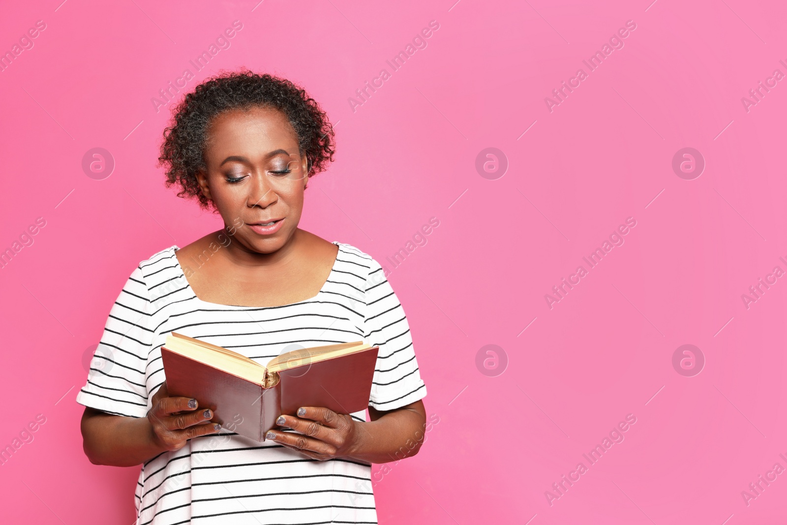 Photo of Portrait of mature African-American woman reading book on pink background, space for text