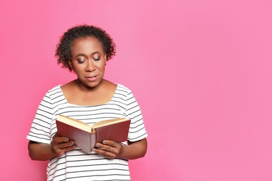 Portrait of mature African-American woman reading book on pink background, space for text