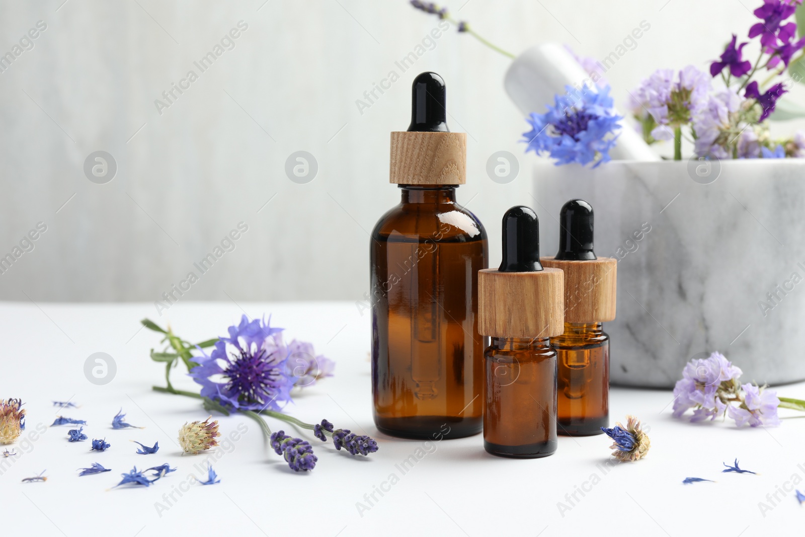 Photo of Aromatherapy. Essential oils, flowers, mortar and pestle on white table