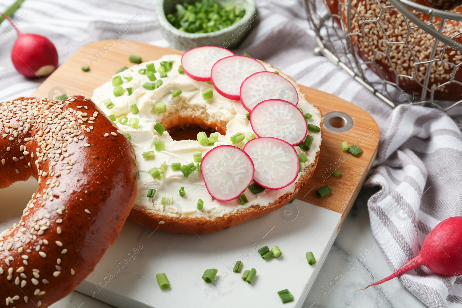 Photo of Delicious bagel with cream cheese, green onion and radish on board, closeup