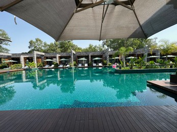 Photo of Swimming pool with wooden deck, exotic plants, umbrellas and sunbeds at luxury resort