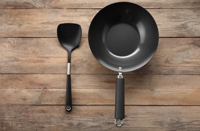 Black metal wok and spatula on wooden table, top view