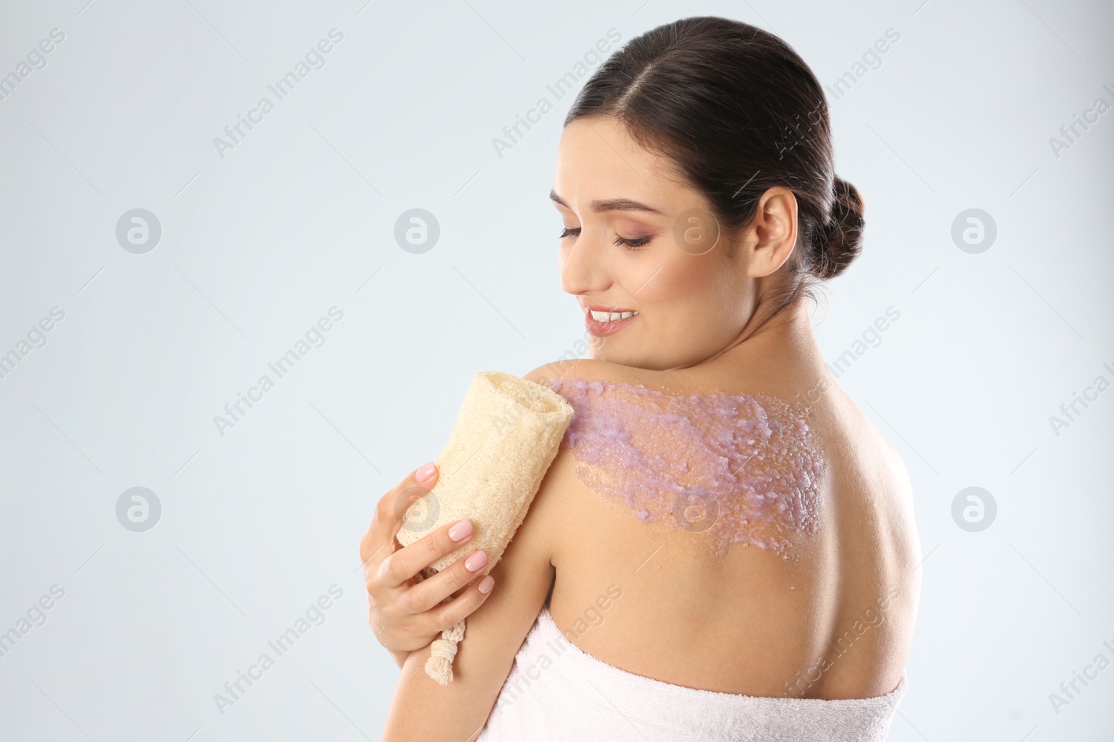 Photo of Young woman applying natural scrub on her body against light background