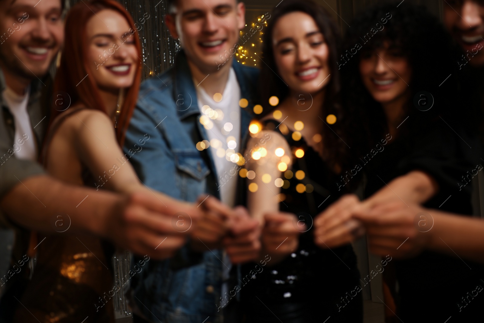 Photo of Blurred view of happy friends with sparklers celebrating birthday indoors