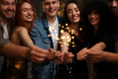 Photo of Blurred view of happy friends with sparklers celebrating birthday indoors