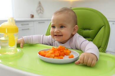 Photo of Cute little baby eating carrot at home, focus on plate