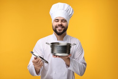 Happy young chef in uniform holding cooking pot on orange background