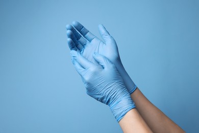 Photo of Doctor wearing medical gloves on light blue background, closeup