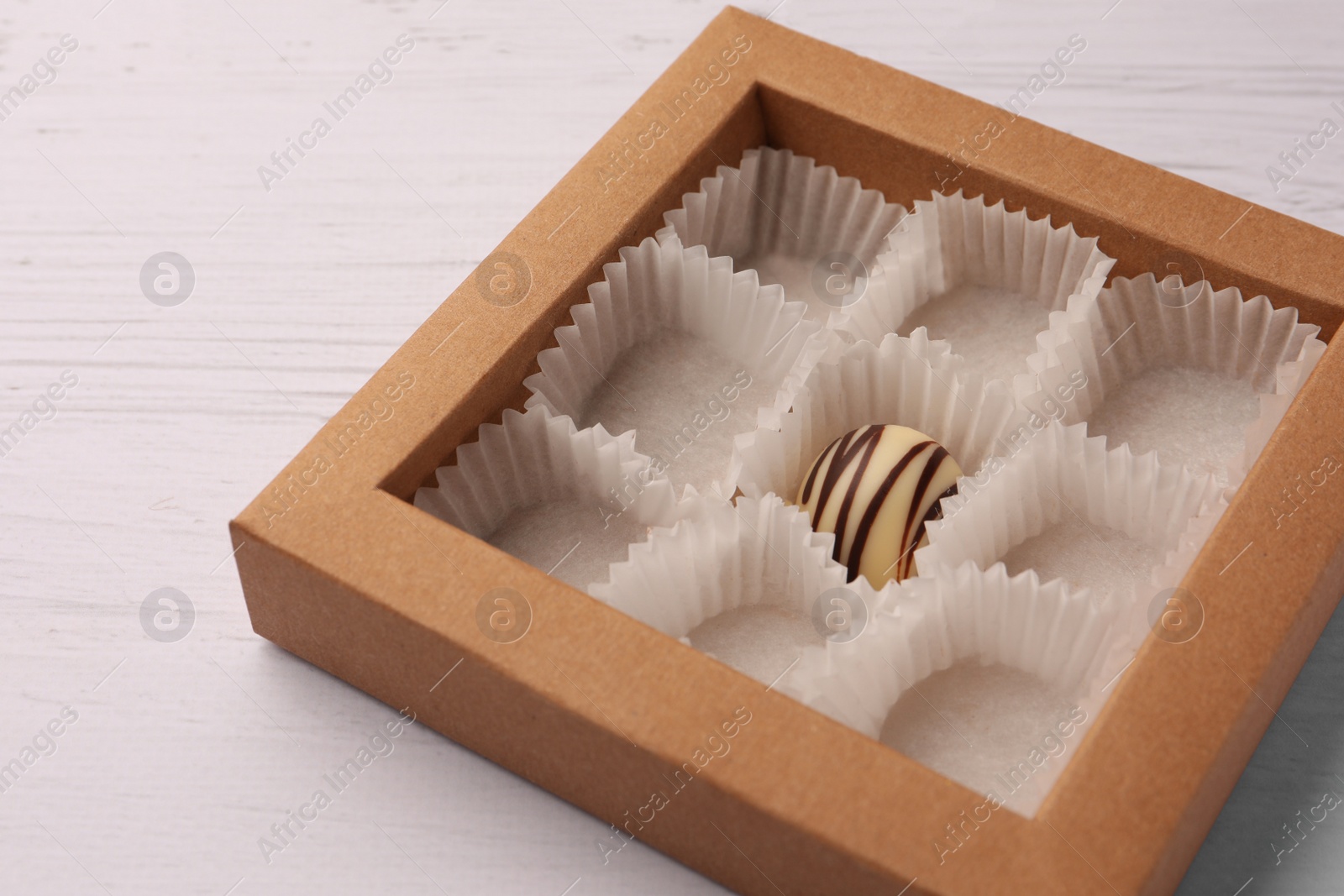 Photo of Partially empty box of chocolate candies on white wooden table, closeup