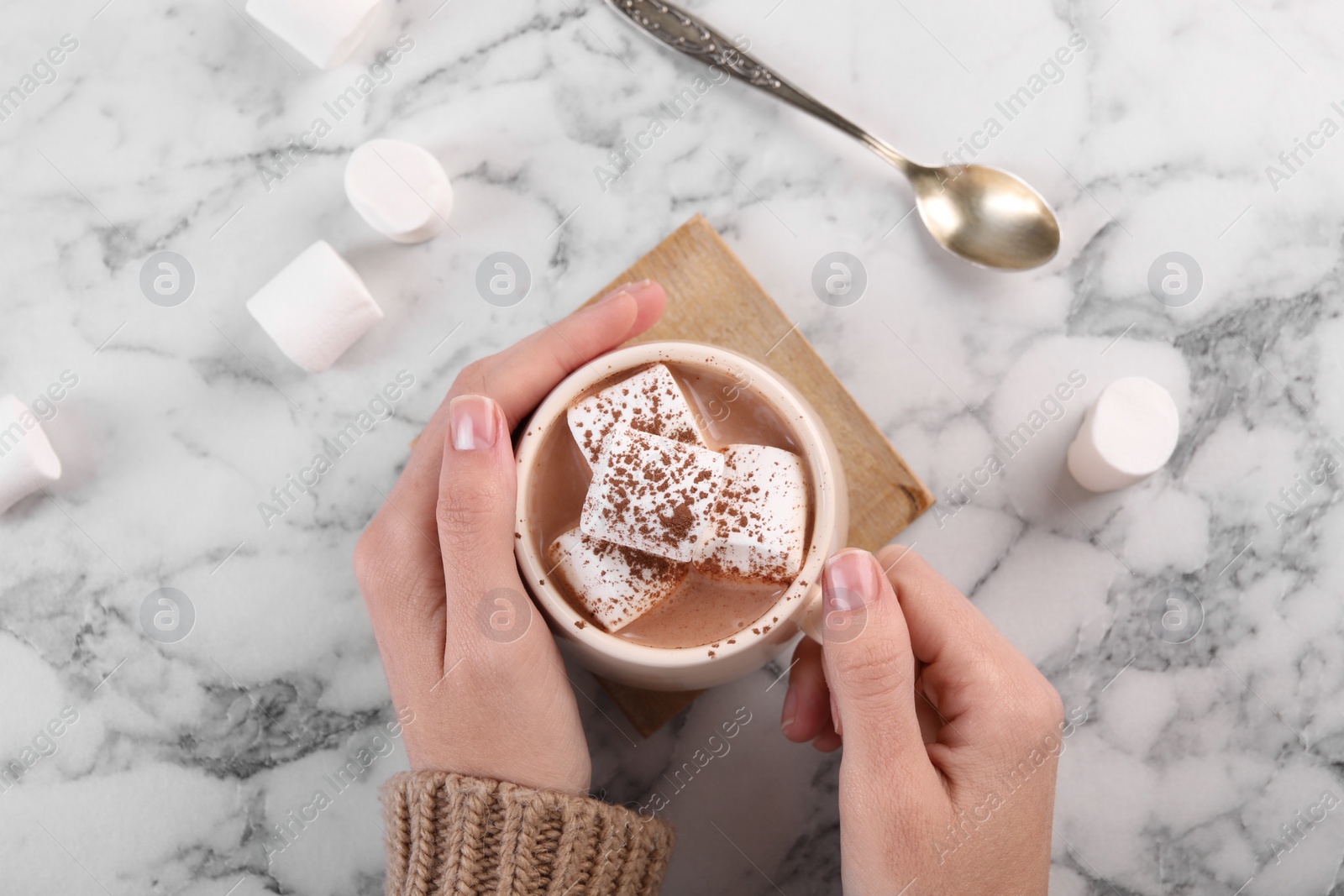 Photo of Woman drinking aromatic hot chocolate with marshmallows and cocoa powder at white marble table, top view