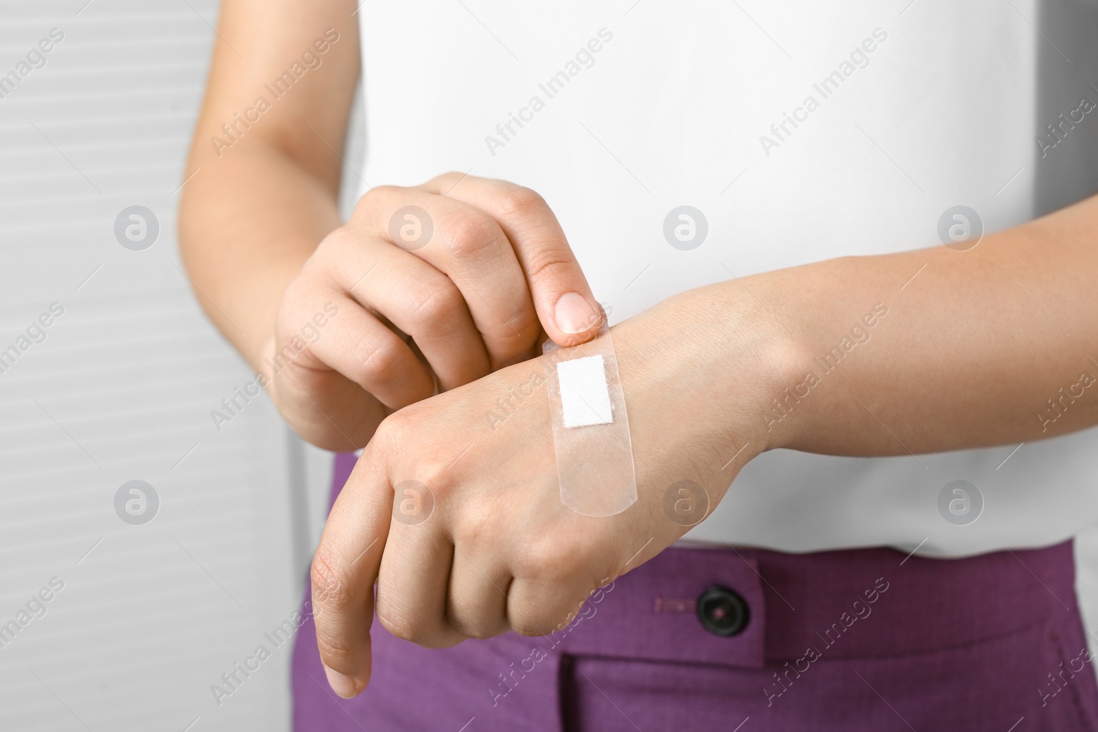 Photo of Female applying plaster on her hand against light background, closeup view