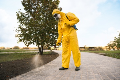 Photo of Person in hazmat suit disinfecting street pavement with sprayer. Surface treatment during coronavirus pandemic