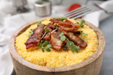 Photo of Cooked cornmeal with bacon and microgreens in bowl on light table, closeup