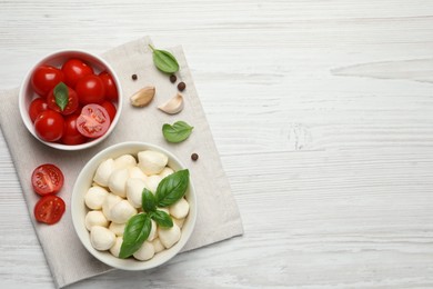 Photo of Delicious mozzarella balls in bowl, tomatoes and garlic on white wooden table, flat lay. Space for text