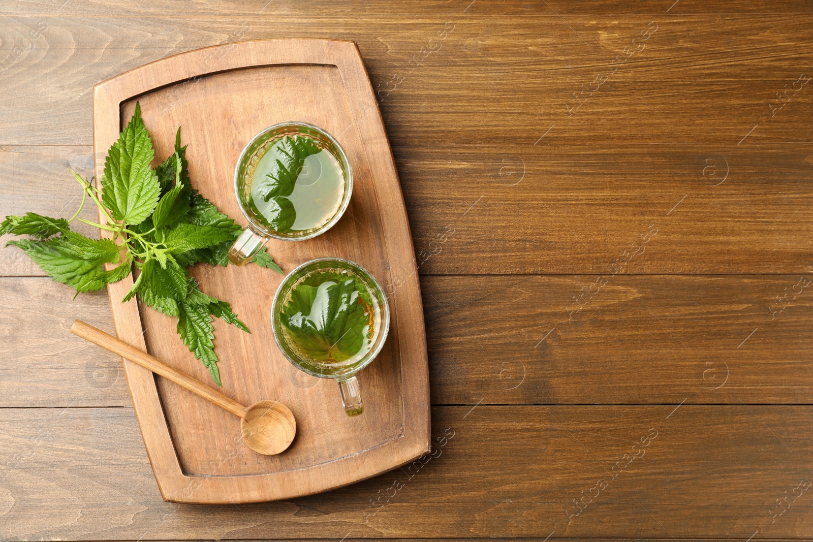 Photo of Glass cups of aromatic nettle tea and green leaves on wooden table, top view. Space for text